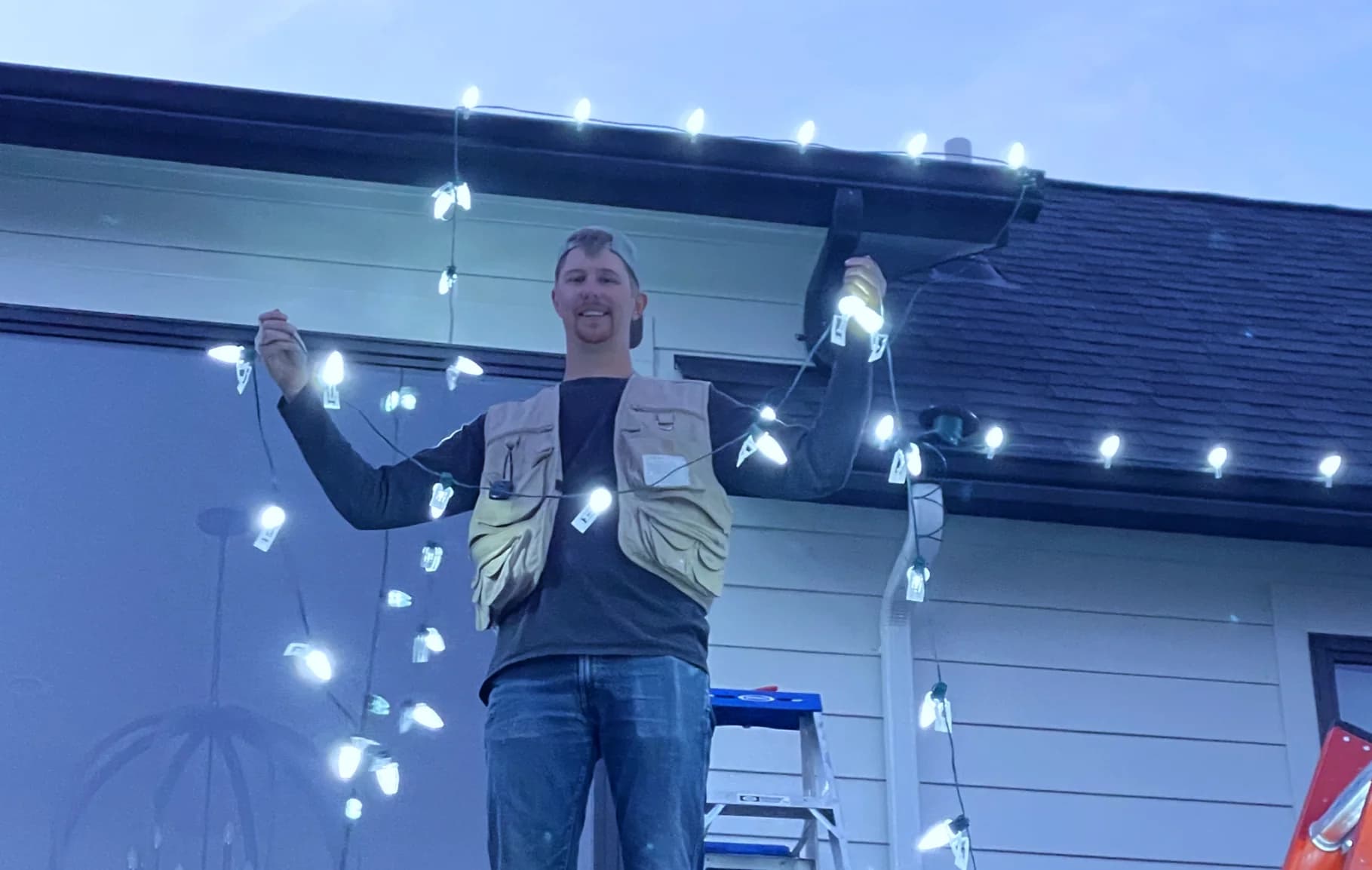 Crew member on a ladder handling a strand of lights at a home's roofline