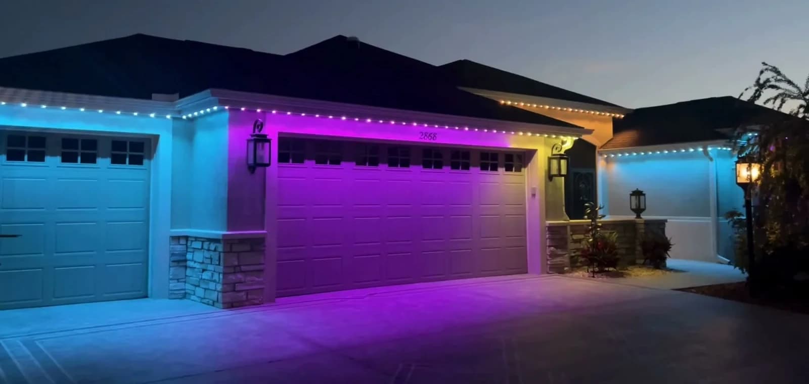 Home at dusk with permanent RGB lights under the roofline washing the garage in blue and purple