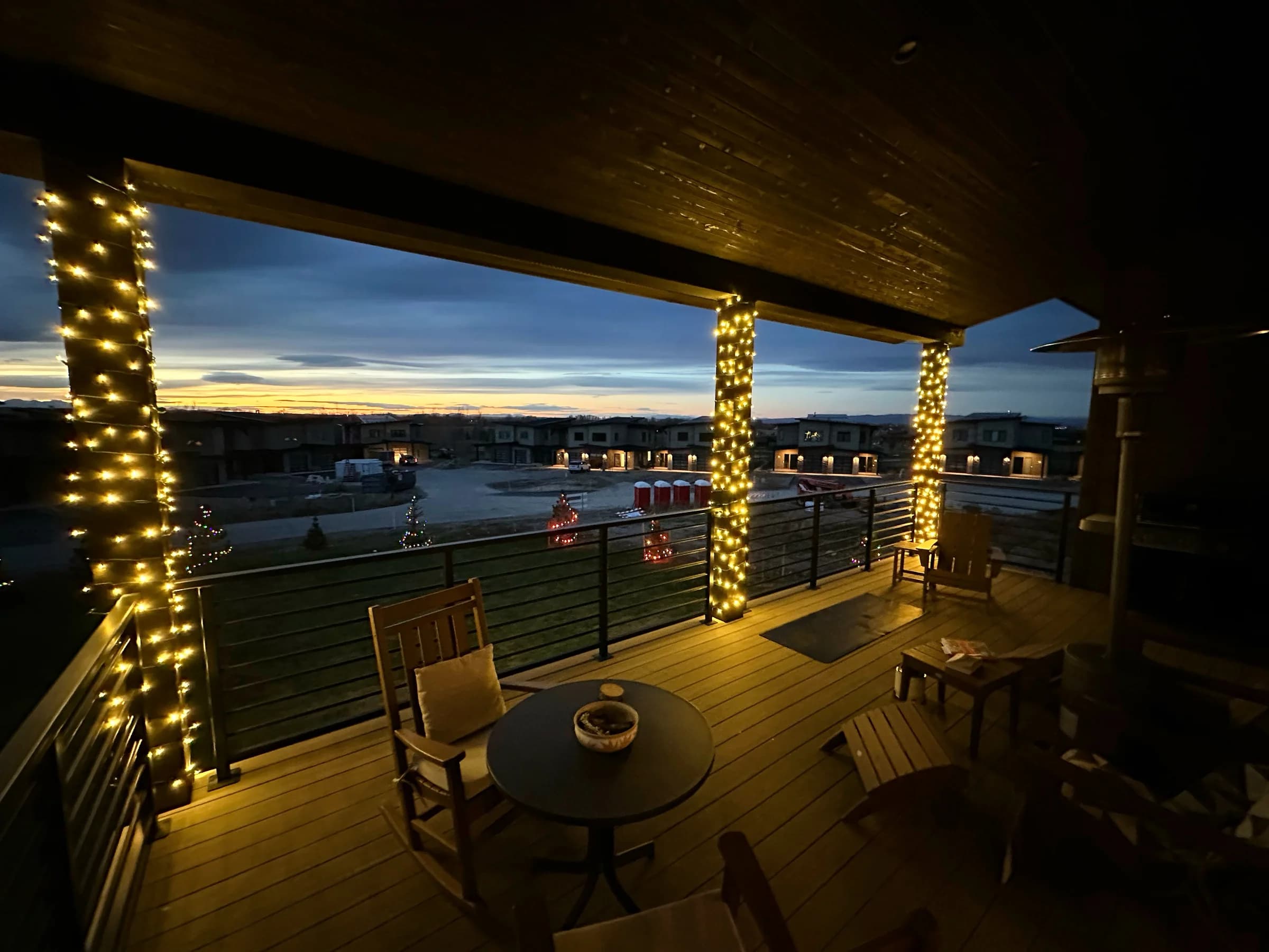 Covered deck with columns wrapped in warm white lights, looking out at a winter sunset