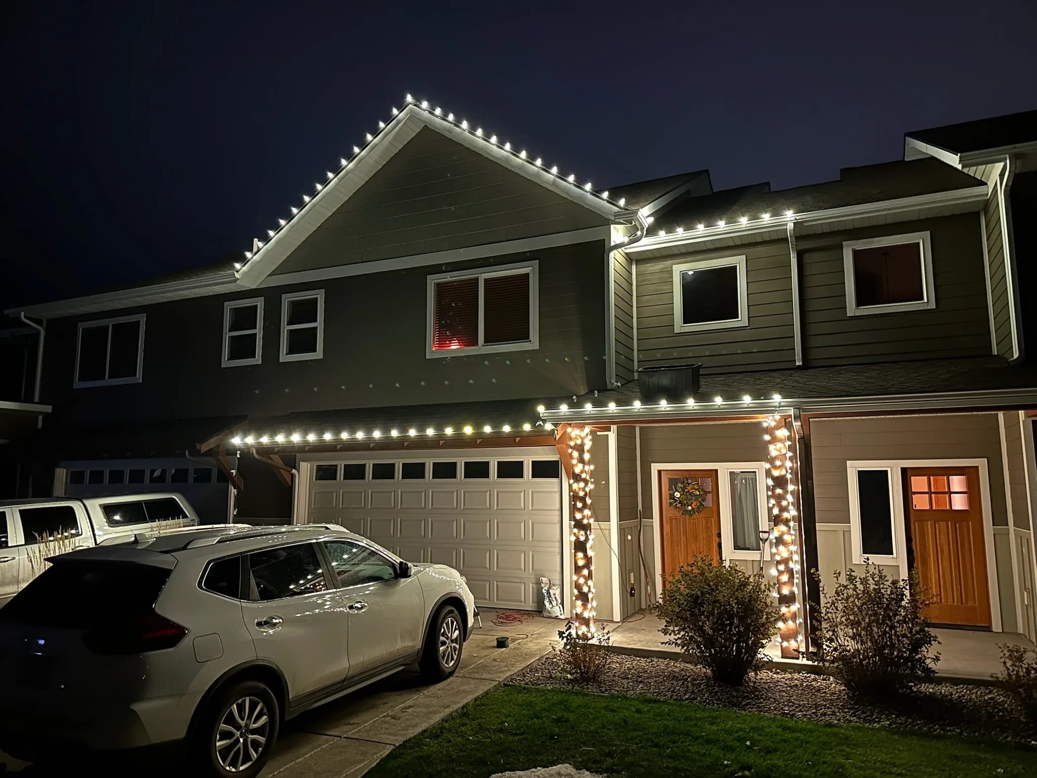 Two-story home with white lights along each roofline and porch pillars wrapped in white lights